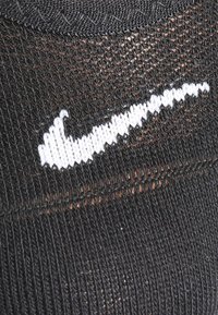 Crna atletska čarapa s bijelim izvezenim Nike logom, s teksturiranim materijalom i čvrstim prianjanjem oko gležnja.