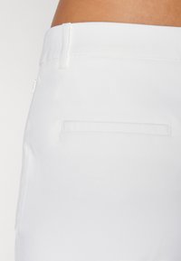 Λευκά παντελόνια με λεία, ματ υφή. Διαθέτουν μια κλασική πίσω τσέπη με καθαρό τελείωμα ραφής και θηλιές ζώνης στη μέση.