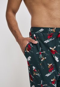 Groene pyjamabroek met een feestelijk patroon van moose in winterkleding, met een tailleband met trekkoord en zijzakken. Zacht, lichtgewicht stof.