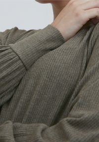 Maglione a coste verde oliva con maniche lunghe, caratterizzato da una morbida texture e un fit rilassato, con tessuto drappeggiato sulle spalle.