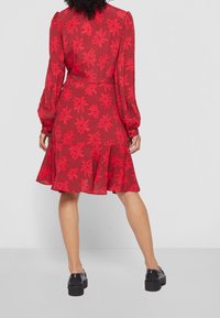 Robe à motif floral rouge avec de longues manches bouffantes et une jupe évasée. Fabriquée en tissu léger, avec une taille bien cintrée et des détails en boutons.