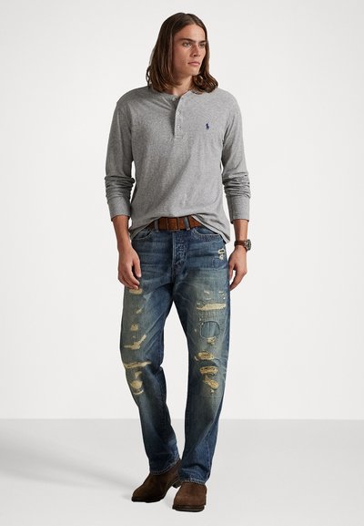 Γκρι μακρυμάνικο πουκάμισο henley με κουμπωτή λαιμόκοψη, σε συνδυασμό με φθαρμένα μπλε τζην που διαθέτουν τριμμένα κομμάτια και καφέ δερμάτινη ζώνη.
