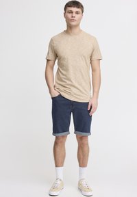 Bēša īsroku T-krekls ar tekstūru kopā ar tumšām džinsa šortiem, salocītiem apkašdaļas galiem, baltām zeķēm un bēšām sporta kurpēm. Vienkārša, ikdienišķa apģērba izvēle.