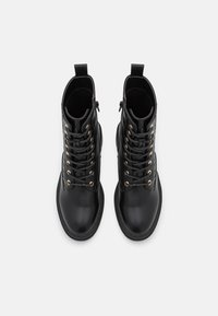 Botas de tobillo de cuero negro con herrajes dorados, cordones y cremalleras laterales. Textura suave con punta redondeada y suela plana.
