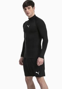 Fekete sportos hosszúujjú póló fitted fazonnal és magas gallérral, fekete rövidnadrággal párosítva. Mindkét darabon fehér Puma logó található.