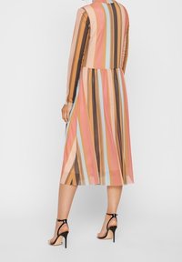 Długa sukienka z pionowymi paskami w odcieniach różu, brązu i niebieskiego. Wykonana z przezroczystego materiału z długimi rękawami i rozkloszowanym dołem. Czarne szpilki.