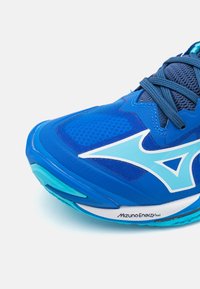 Plava sportska cipela s svijetloplavim Mizuno logotipom, tamnoplave vezice i natpisom "Mizuno Energy nxt" na bijelom međusolu.