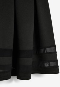 Czarna spódnica o teksturowanym wyglądzie, z paskowymi elementami z siateczki i gładkim wykończeniem materiału. Dolna krawędź jest lekko rozkloszowana.