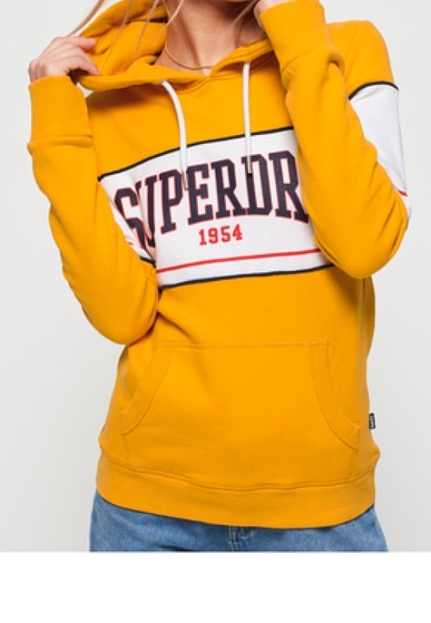 Sudadera amarilla con capucha y bolsillo frontal, con una franja horizontal blanca y roja que lleva el texto "SUPERDRY 1954" en el centro.