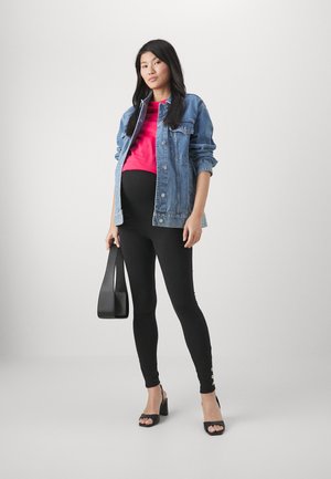 Denimjakke, pink top, sorte leggings med guldknapdetaljer og sorte hælede sandaler. Modellen holder en sort taske.