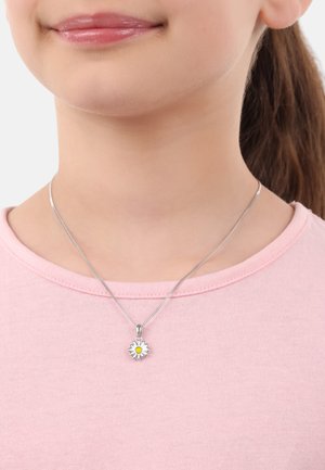 Collar de cadena de plata con un colgante de margarita que presenta una flor blanca y un centro amarillo, llevado sobre una camiseta de cuello redondo rosa claro.