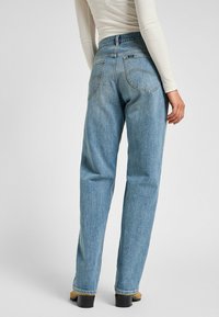Jeans in denim di colore blu chiaro, a vita alta, con taglio dritto, cuciture visibili, tasche posteriori e vestibilità rilassata sui pantaloni.