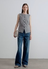 Γκρι αμάνικο τοπ με κουμπιά μπροστά, σε συνδυασμό με ψηλόμεσα φαρδιά τζιν παντελόνια και μία μικρή, ανοιχτόχρωμη τσάντα. Ομαλή υφή.