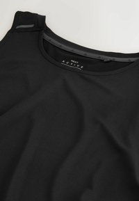 Haut de sport noir sans manches avec col rond et étiquette "Next Active" à l'intérieur du col.
