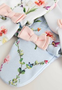 Morbidi guantini per neonati con stampe floreali, decorati con fiocchi di tessuto rosa chiaro su sfondi azzurro pastello e bianco.