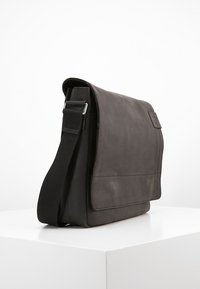 Borsa a tracolla in pelle nera con finitura testurizzata, tracolla regolabile e chiusura a pattina. Caratterizzata da una tasca frontale singola e bordi lisci.