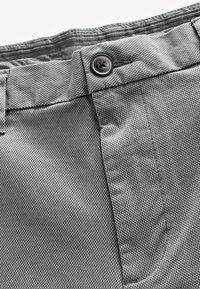 Shorts en tissu texturé gris avec fermeture à bouton en métal et couture détaillée. Le matériau présente un motif tissé fin.