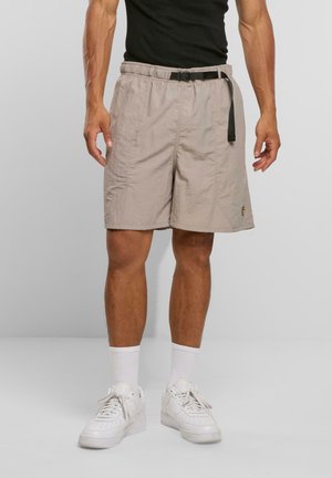 Helle beige Shorts mit einem elastischen Bund, einem verstellbaren schwarzen Gürtel und seitlichen Taschen. Glattes, leichtes Material. Getragen mit weißen Sneakern.
