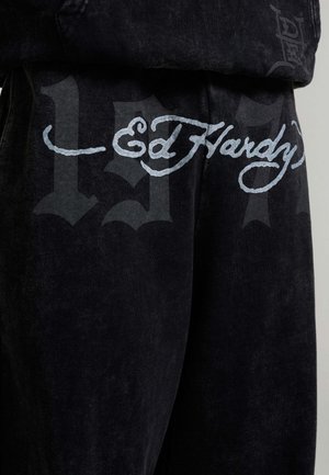 Ed Hardy zwart stof met lichtgrijze schrift "Ed Hardy" en grote, vage donkergrijze gotische cijfers op de achtergrond.