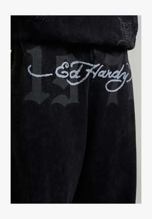 Ed Hardy zwart stof met lichtgrijze schrift "Ed Hardy" en grote, vage donkergrijze gotische cijfers op de achtergrond.