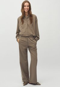 Beige tvådelad outfit med en knäppbar topp i kort modell och löst sittande byxor med elastisk midja och sidodetaljer.