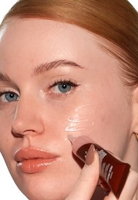 Se está aplicando un gel transparente sobre la piel utilizando un tubo transparente con una etiqueta marrón oscura. La piel parece suave con una iluminación suave.