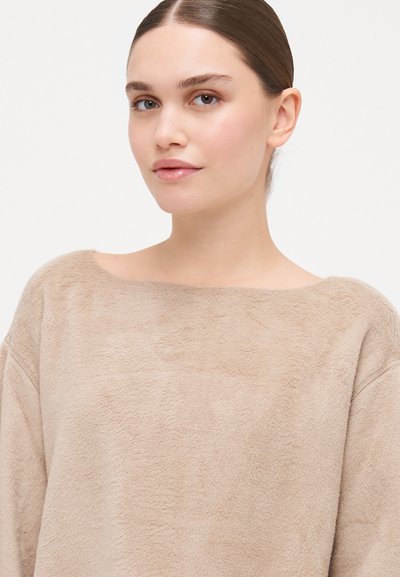 Beige fleece sweater with a wide boat neck, soft texture, and loose fit. The fabric appears plush and comfortable with minimal seams.