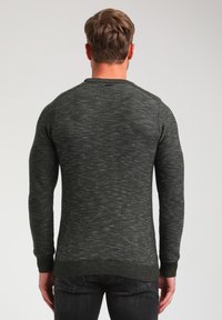 Pull en maille vert foncé avec une finition texturée, des poignets et un ourlet côtelés. Doté d'un col rond et d'une silhouette ajustée.