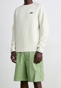 Ljusgrön sweatshirt med svart Nike-logga; har raglanärmar och en mjuk textur. Matchas med ljusgröna cargoshorts.