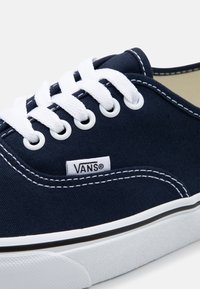 Marinblå canvas sneaker med vita snören, med gummisula, svart randdetalj och en liten logotagg på sidan.