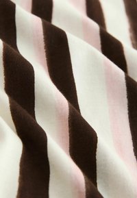 Zbliżenie na tkaninę o falistej fakturze z pionowymi paskami w kolorach ciemnobrązowym, białym i jasnoróżowym.