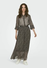 Schwarzes florales Maxikleid mit Knopfleiste, langen Ärmeln und gebundenem Taillengürtel; verfügt über eine durchsichtige Textur und einen schichtweisen Fall. Getragen mit weißen Sneakers.