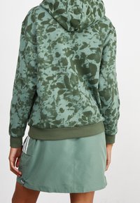 Grön hoodie med ett tie-dye-mönster, med huva och ribbad nederkant. Matchad med en grön kjol som har en sidficka och detaljer.