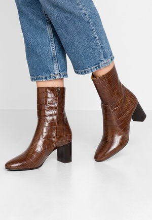 Bruine enkellaarsjes met krokodillenprint en blokhakken, gedragen met cropped blauwe jeans op een lichte vloer.