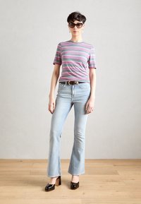 Camiseta de rayas de manga corta en púrpura, azul y rosa; vaqueros acampanados de color azul claro; zapatos de tacón cuadrado marrones; gafas de sol negras de gran tamaño.