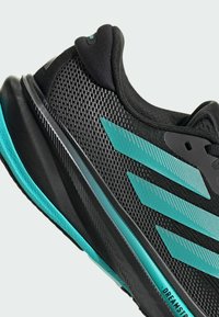 Černá sportovní bota s tyrkysovými akcenty. Disponuje strukturovaným síťovaným svrškem, dynamickým pruhovaným designem a polstrovanou podrážkou s elegantním povrchem.