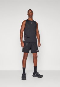 Completo sportivo composto da canottiera nera e pantaloni corto con un design aderente, dettagli rossi e pannelli in rete traspirante. Indossato con sneakers nere e calzini.