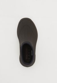 Zapato negro impermeable tipo slip-on con detalles de costura elevada y puntera redondeada, fotografiado desde arriba sobre un fondo blanco.
