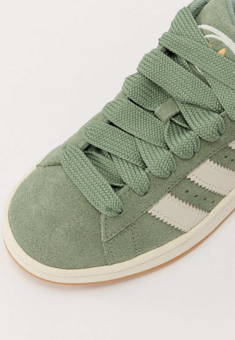 Zapatillas de ante verde con cordones trenzados, que cuentan con tres rayas blancas a lo largo del costado y una suela de goma clara. Diseño de puntera redondeada.