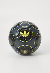 Čierny futbalový loptu s modrými a žltými zakrivenými pruhmi, žltým logom Adidas a erbom Manchester United na bielom pozadí.