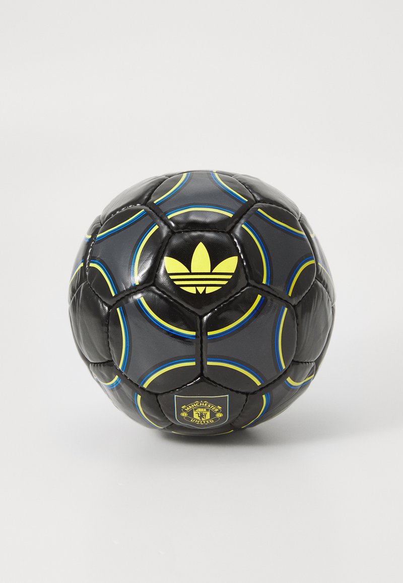 Čierny futbalový loptu s modrými a žltými zakrivenými pruhmi, žltým logom Adidas a erbom Manchester United na bielom pozadí.