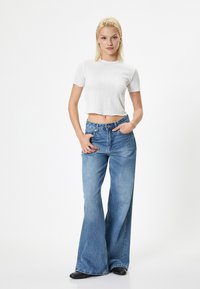 Biały prążkowany crop top z krótkim rękawem w połączeniu z jasnoniebieskimi spodniami typu wide-leg, z guzikami i zamkiem błyskawicznym oraz bocznymi kieszeniami.