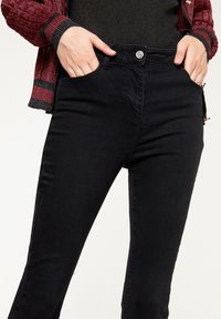 Jeans negros con un diseño ajustado, que cuentan con bolsillos delanteros, cierre de botón y una textura de denim suave.