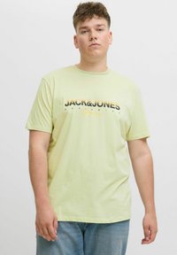 Hellgrünes T-Shirt mit kurzen Ärmeln aus Baumwolle, das einen schwarz-orangefarbenen Grafikdruck mit der Aufschrift "JACK&JONES" auf der Vorderseite zeigt.