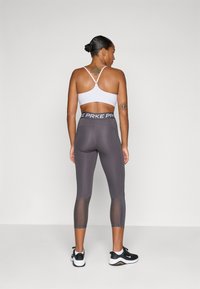 Grijze sportleggings met mesh-panelen en een zwarte tailleband met de tekst "NIKE PRKE." Draagt een witte sport-bh en zwarte sneakers.
