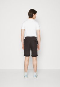 Shorts en coton noir avec ourlets roulés, dotés de poches latérales. Assortis à un t-shirt blanc uni et des chaussures de sport bleu clair.