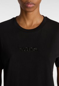 Maglietta nera in cotone con collo a giro e logo "vans." in rilievo in filo nero abbinato sulla parte anteriore. Maniche corte, colletto a costine.