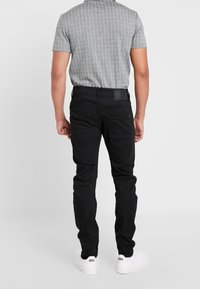 Svarta denimjeans med slim fit, med kontrasterande sömmar och två bakfickor, i kombination med en grå randig kortärmad skjorta.