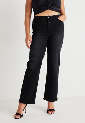 Black high-waisted jeans with a straight-leg cut, made from denim, featuring front pockets and a button closure. Worn with strappy black heels.