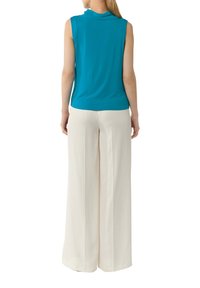 Top bez rękawów w turkusowym kolorze z delikatnym dekoltem w cowl, zestawiony z białymi spodniami o wysokim stanie i szerokich nogawkach. Gładka tekstura z miękkim układem.